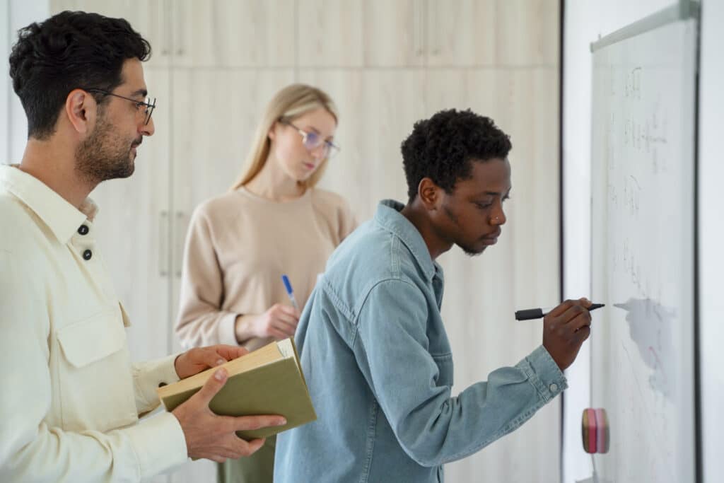 Jovem empreendedor, escrevendo em um quadro branco acompanhado de mais dois colegas de trabalho.